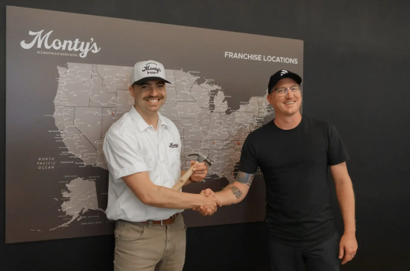 Monty's Handyman franchise owners shaking hands in front of US franchise locations map